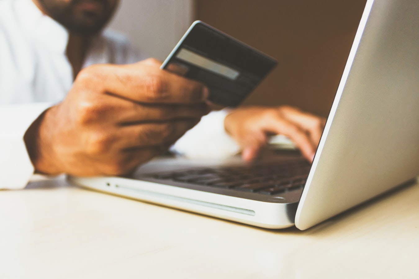 closeup of two hands, one holding a credit card and one typing on a macbook keyboard